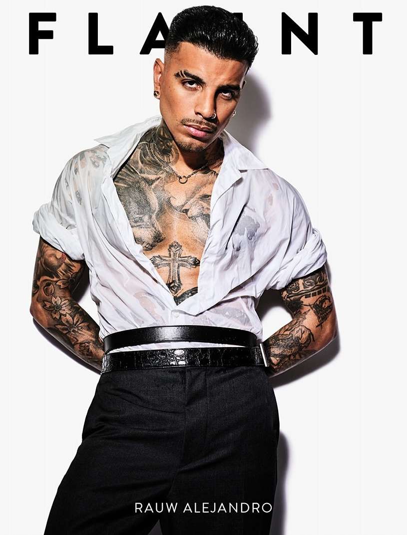 Close-up studio shot of tattooed adult male in open wet white shirt and black pants, posing against a clean white background.
