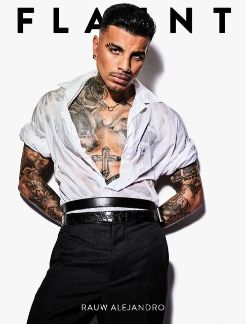 Close-up studio shot of tattooed adult male in open wet white shirt and black pants, posing against a clean white background. 