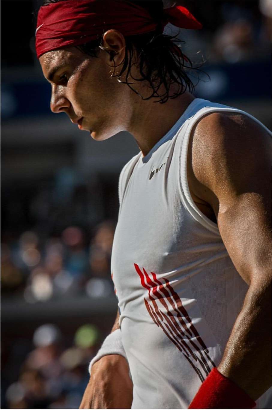 Tennis player wearing a red headband and white tank on court during a match, captured in a close-up shot.