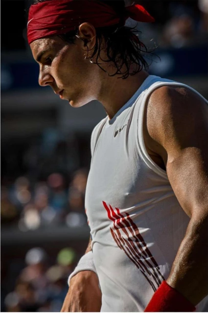 Tennis player wearing a red headband and white tank on court during a match, captured in a close-up shot.