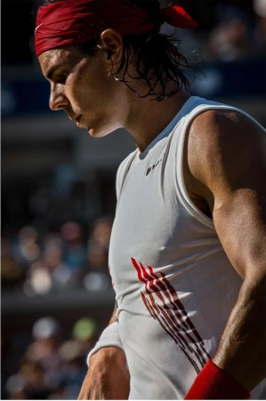 Tennis player wearing a red headband and white tank on court during a match, captured in a close-up shot.