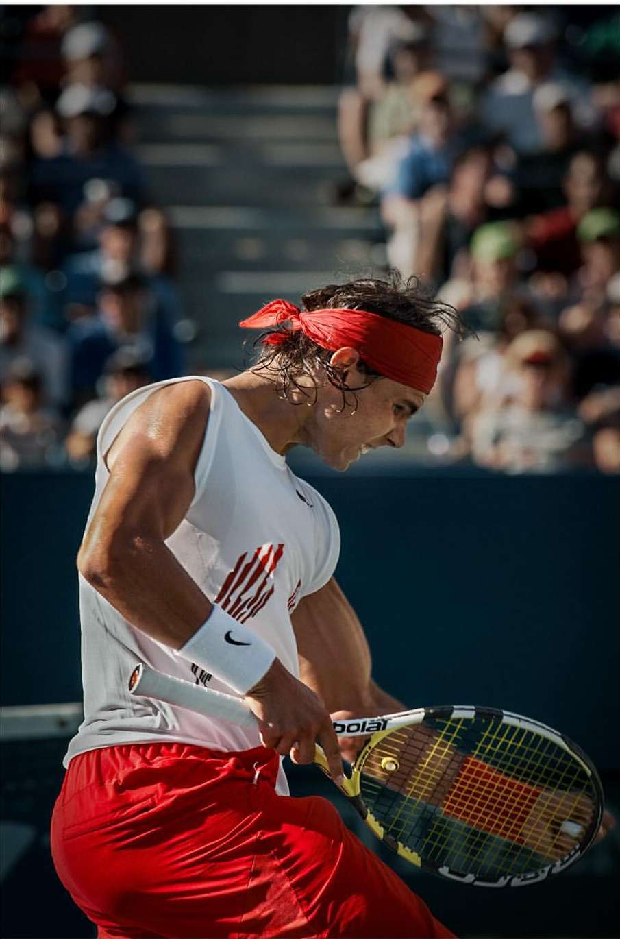 Professional tennis player with red headband in action on outdoor tennis court, focused and determined during a match.