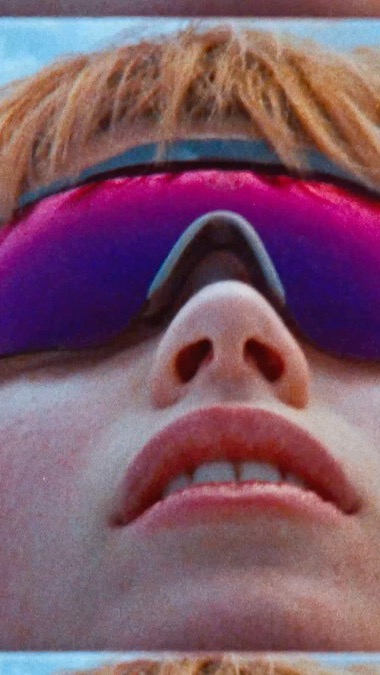 Extreme close-up shot of a face with vibrant pink sunglasses, blonde hair, and fair skin. Bright, evenly distributed lighting.