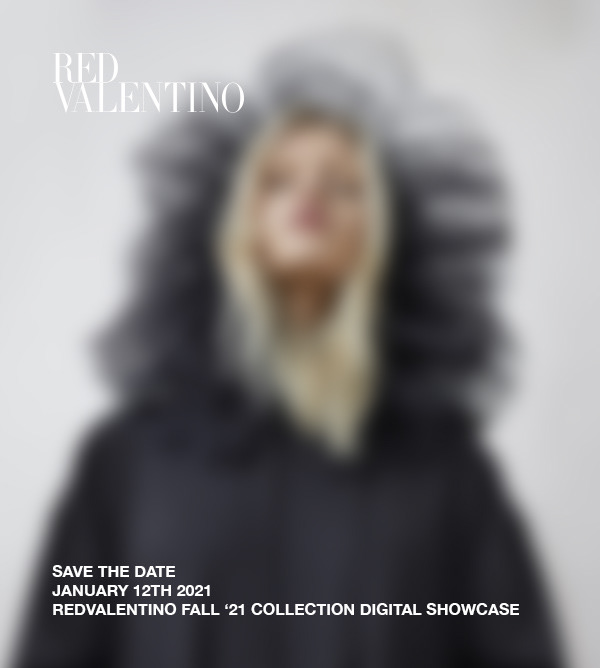 Fashion brand ad featuring a blurry image of a female model wearing a dark dress and black tulle headpiece against a white background.