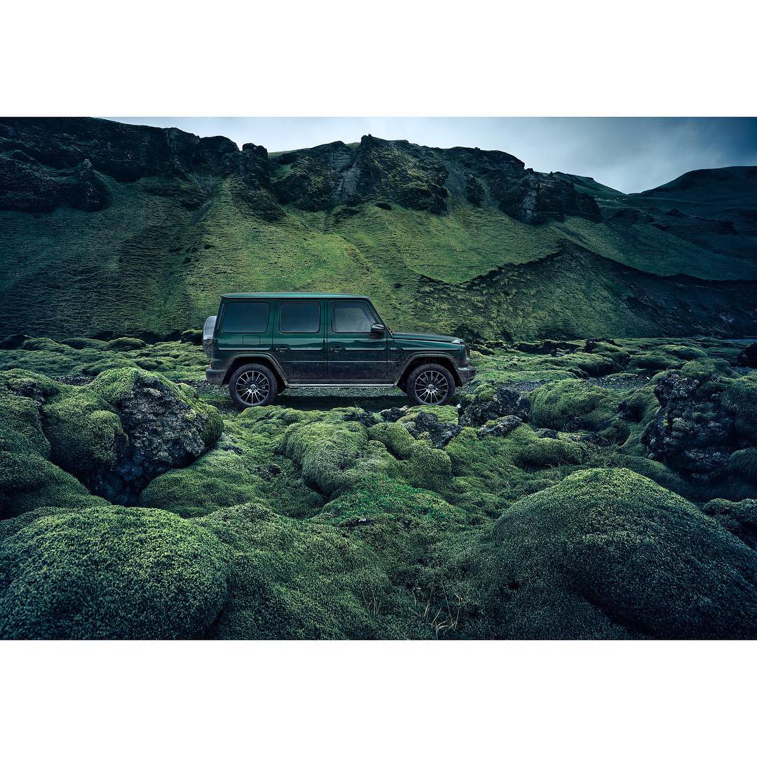Dark green SUV on mossy terrain with a green mountainous background, creating an adventurous and rugged automotive image.