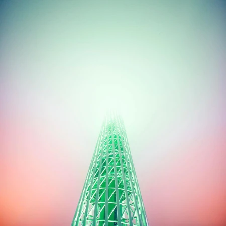 Low angle of a lattice tower disappearing into fog. The structure is green, and the sky is graded from red to green, with fog obscuring the top.