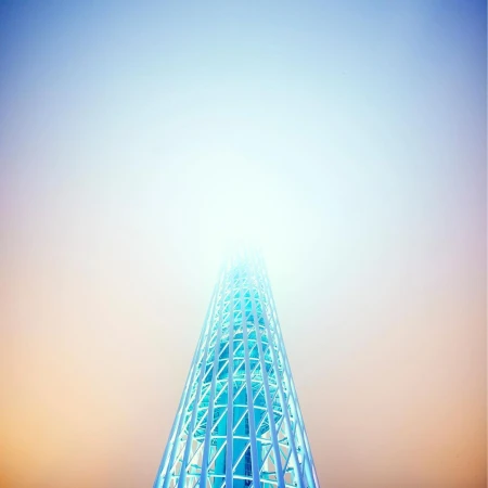 Low-angle shot of a futuristic, blue, steel lattice tower rising through the fog, fading into a bright white sky at daytime.