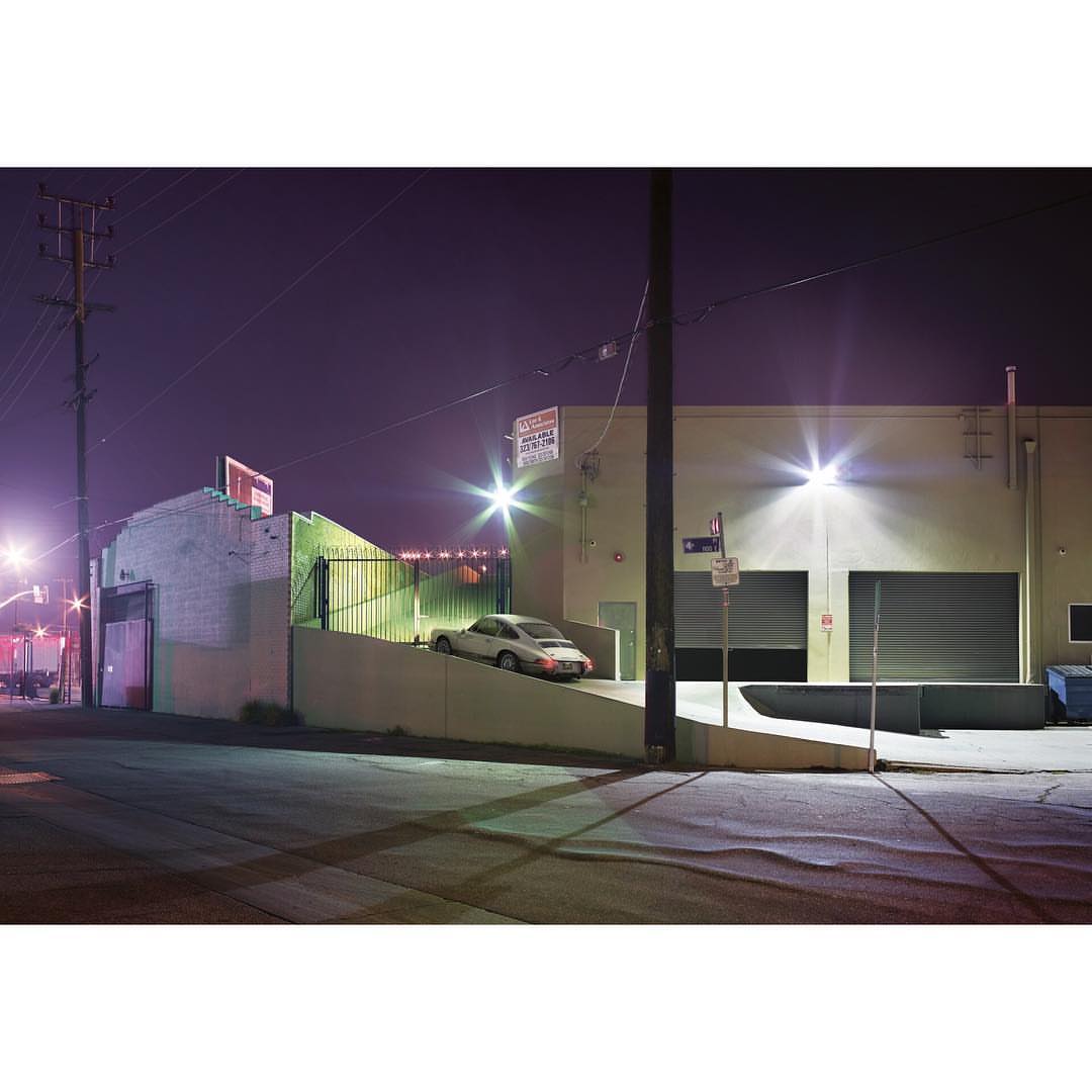 Night scene featuring a silver car parked near a loading dock, illuminated by streetlights, capturing an urban landscape with stark contrasts.
