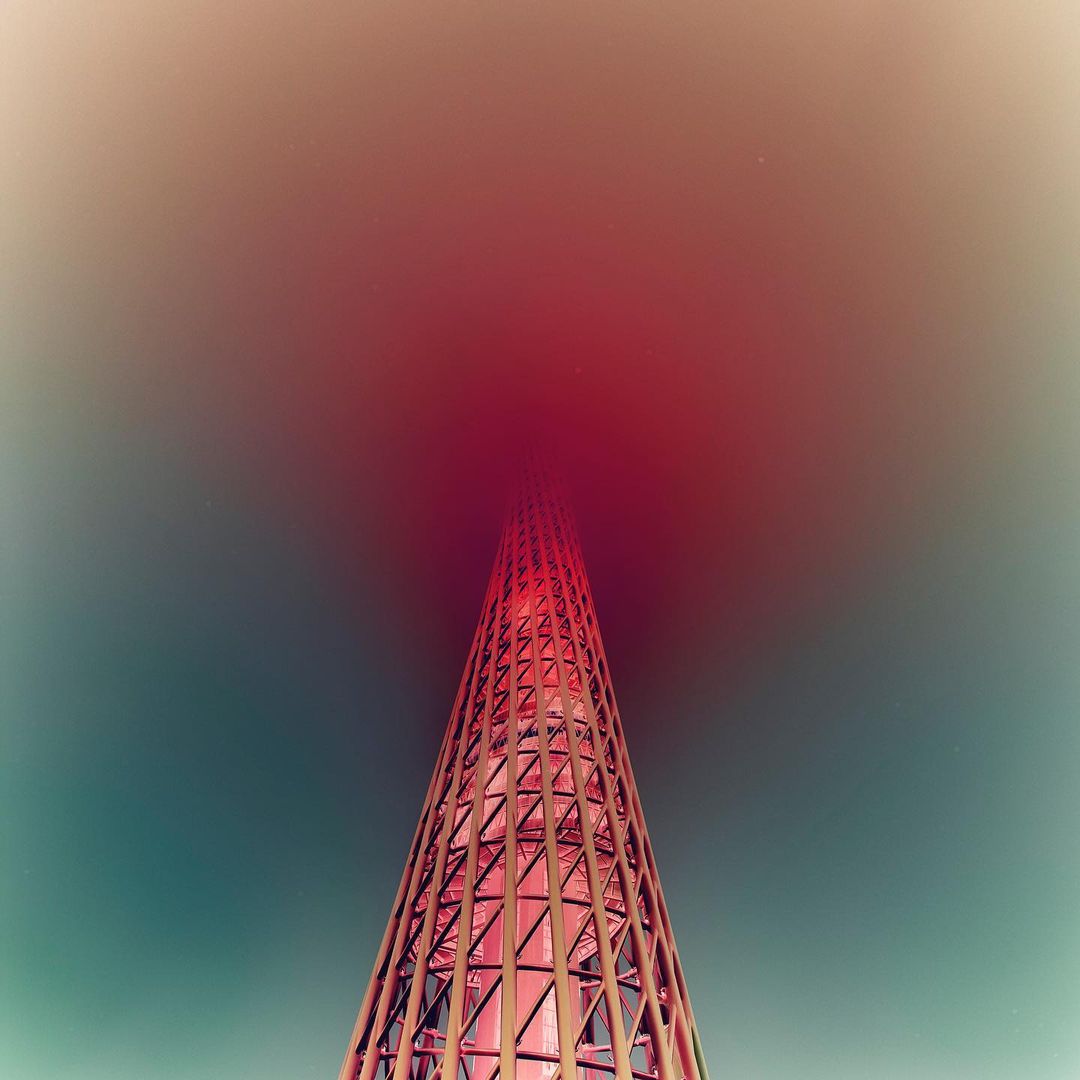 Abstract view of a tall tower-like structure constructed of red metal lattice set against the sky with red color grading.