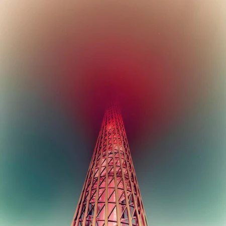 Abstract view of a tall tower-like structure constructed of red metal lattice set against the sky with red color grading.