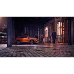 An orange crossover car parked on cobblestone inside a large industrial building with a person walking away.