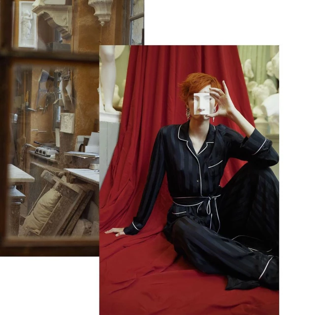 Woman in black pajamas poses with a clear cube in a photo studio with classical busts and a rich red curtain backdrop.