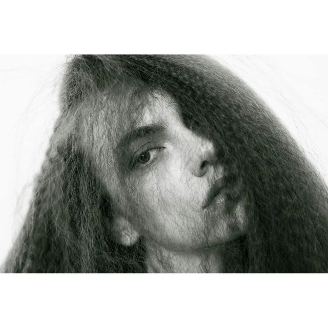 Monochrome portrait of a woman with intricately textured long dark hair framing her face against a stark white backdrop in a beauty shot.