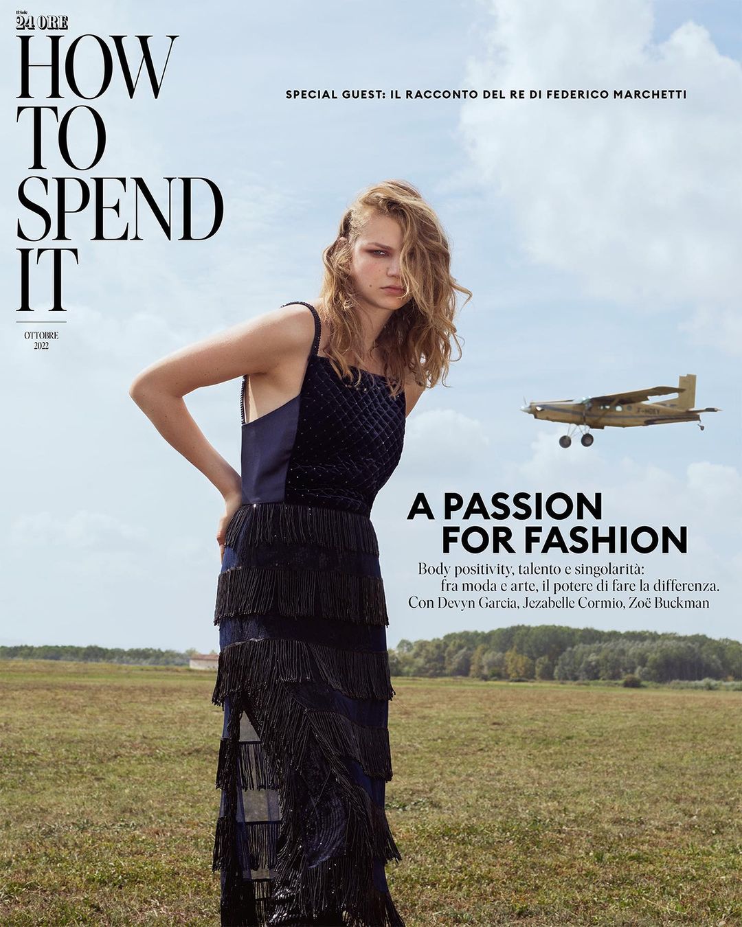 Magazine cover featuring a blonde fashion model in a navy dress with tassels standing in a field with a plane in the distance on a sunny day.