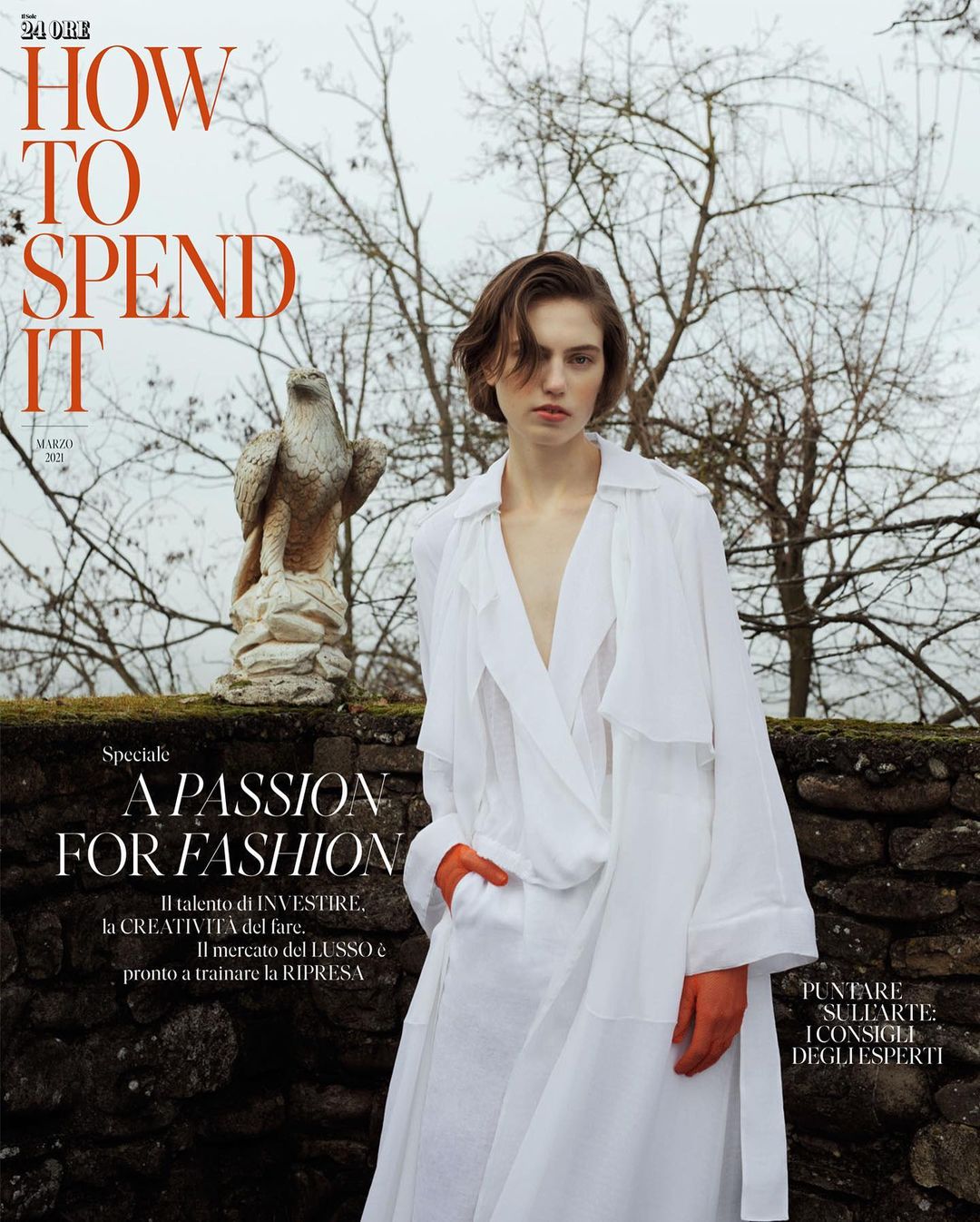 Fashion magazine cover featuring a woman in a white coat, set against an outdoor backdrop with a stone wall and an eagle statue.