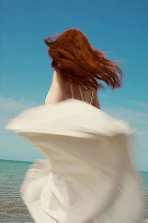 Red-haired woman in a white dress spinning against a blue ocean background