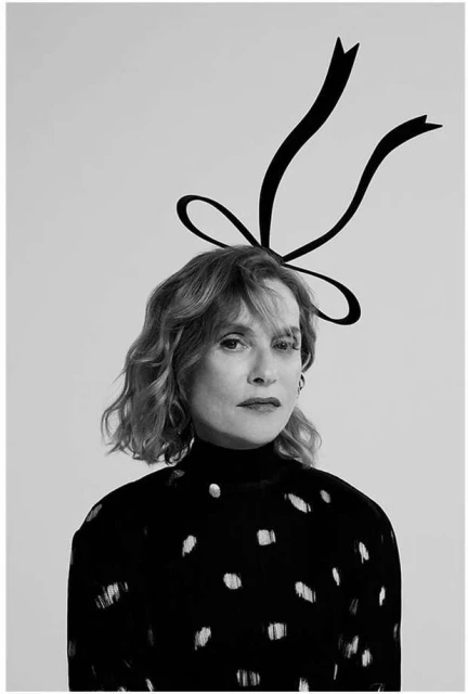 Black-and-white portrait of a woman with fair skin, short blonde hair, wearing a spotted top and a large ribbon headpiece.