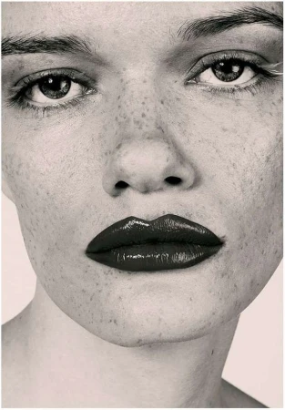 Extreme close up portrait of a woman with heavy freckles and dark glossy lipstick photographed by Marta Bevacqua
