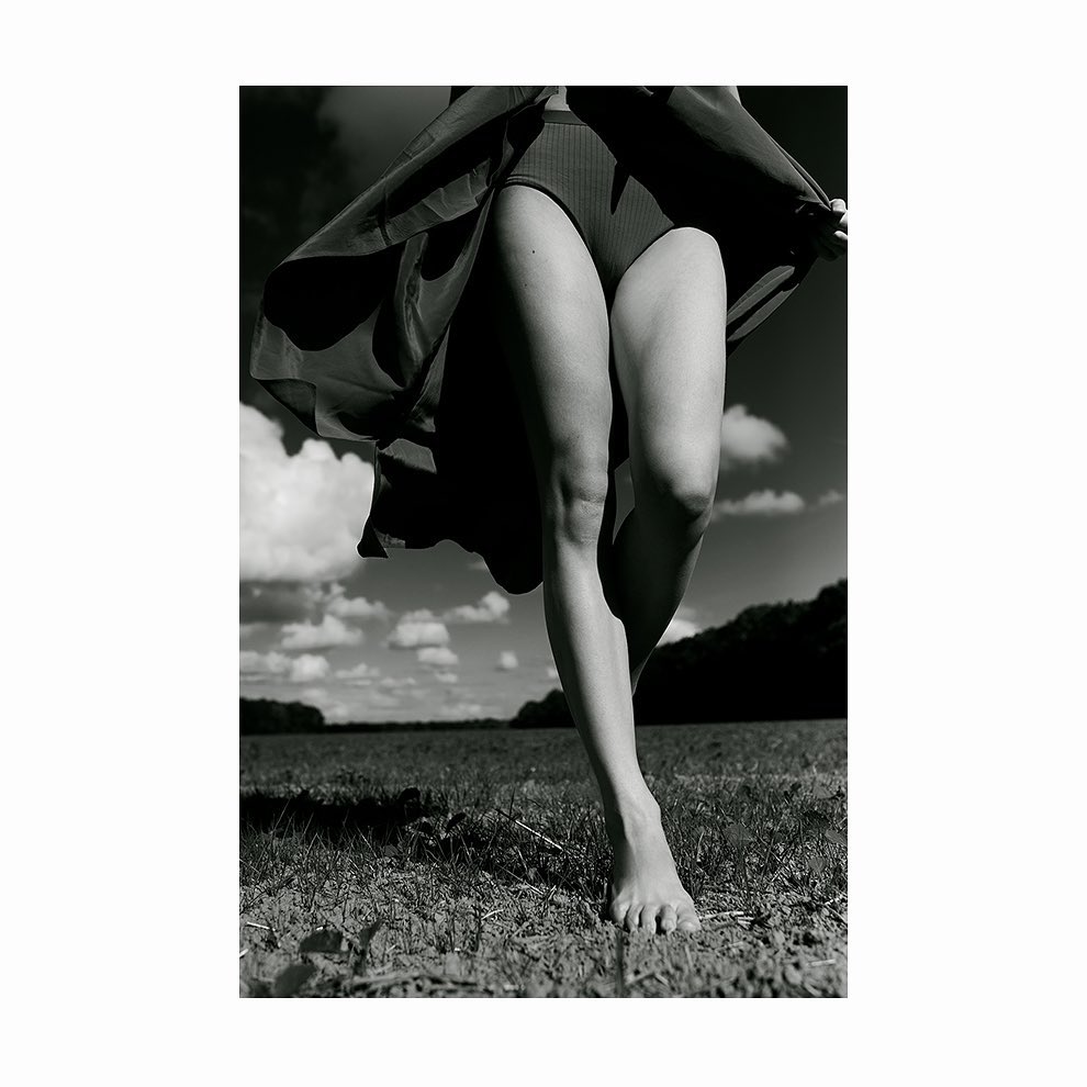 Close-up monochrome photograph of a barefoot woman walking outdoors through a field with flowing skirt.