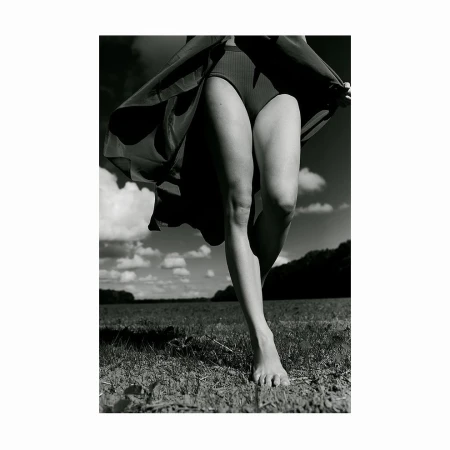 Close-up monochrome photograph of a barefoot woman walking outdoors through a field with flowing skirt.