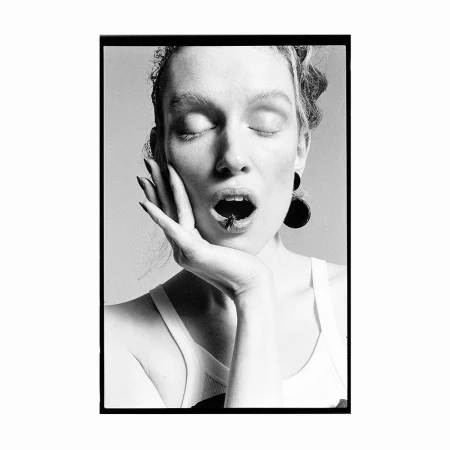 Close-up black and white portrait of a woman with eyes closed, holding her hand to her cheek with a fly on her lips.