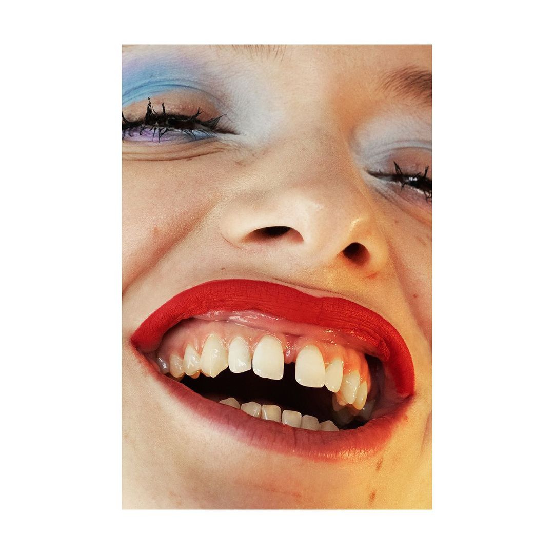 Extreme close-up portrait of a smiling woman with bright red lipstick and blue eye shadow by Marta Bevacqua