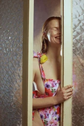 Smiling woman with wet hair wearing a floral dress, seen through a doorway with patterned glass by photographer Marta Bevacqua in Paris.