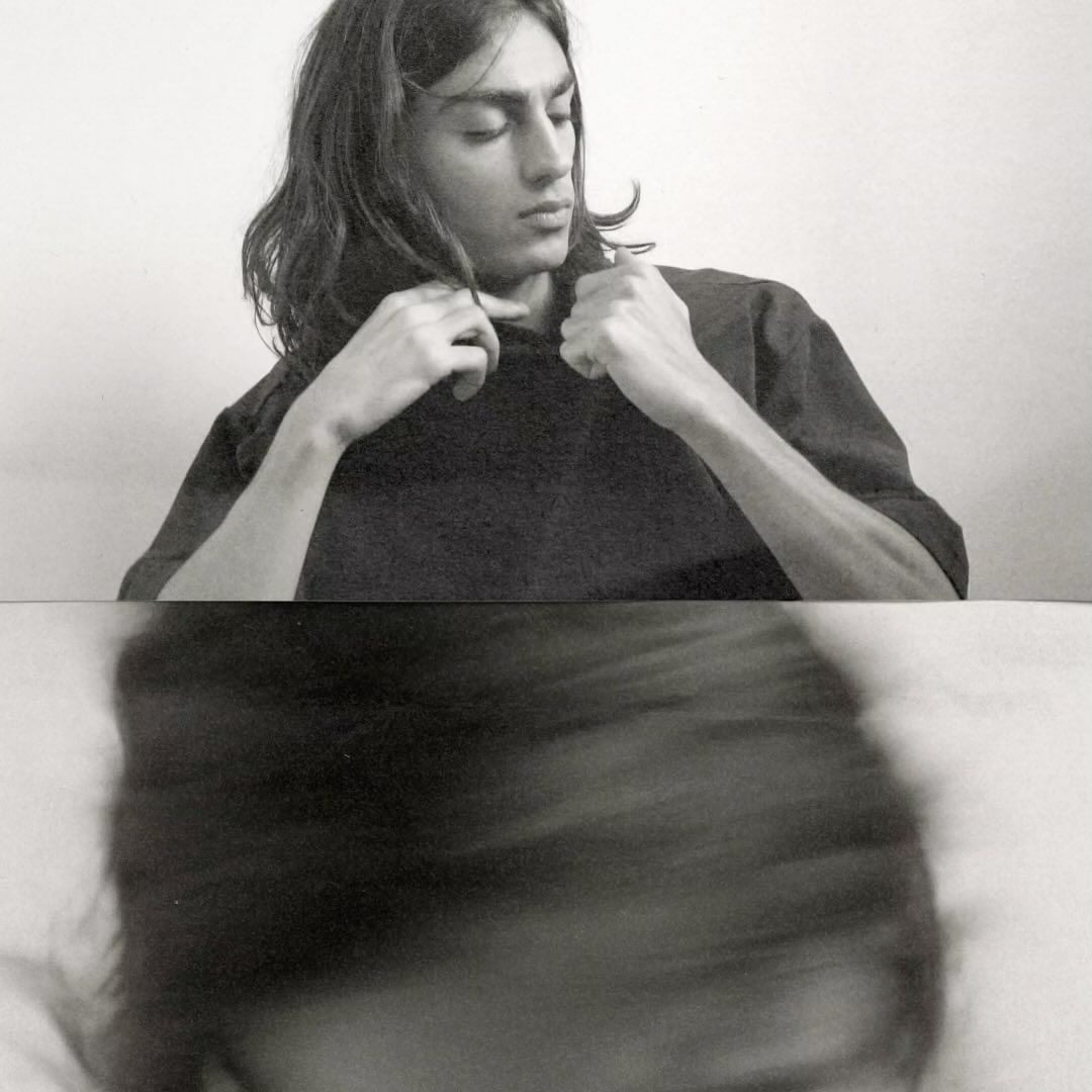 Black and white portrait of a young adult with long hair wearing a dark shirt, captured with a unique blurred effect below.