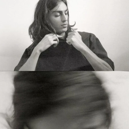 Black and white portrait of a young adult with long hair wearing a dark shirt, captured with a unique blurred effect below.