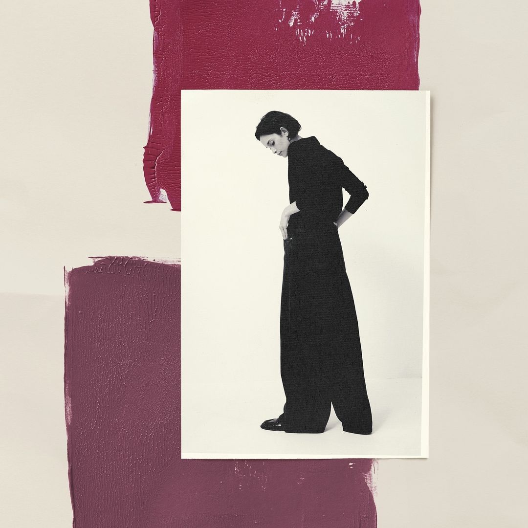 Monochromatic portrait of a woman in dark attire on a bright surface, framed against a backdrop of painted burgundy blocks.