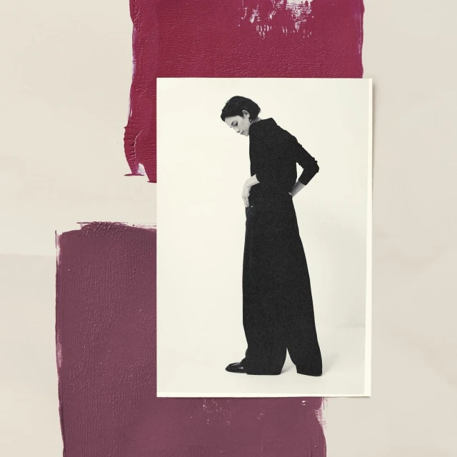 Monochromatic portrait of a woman in dark attire on a bright surface, framed against a backdrop of painted burgundy blocks.