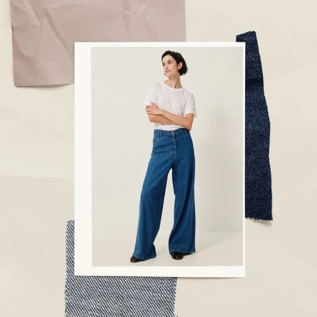 A woman in wide-leg jeans and a white t-shirt poses indoors, framed by fabric swatches. A fashion editorial shot in a studio.