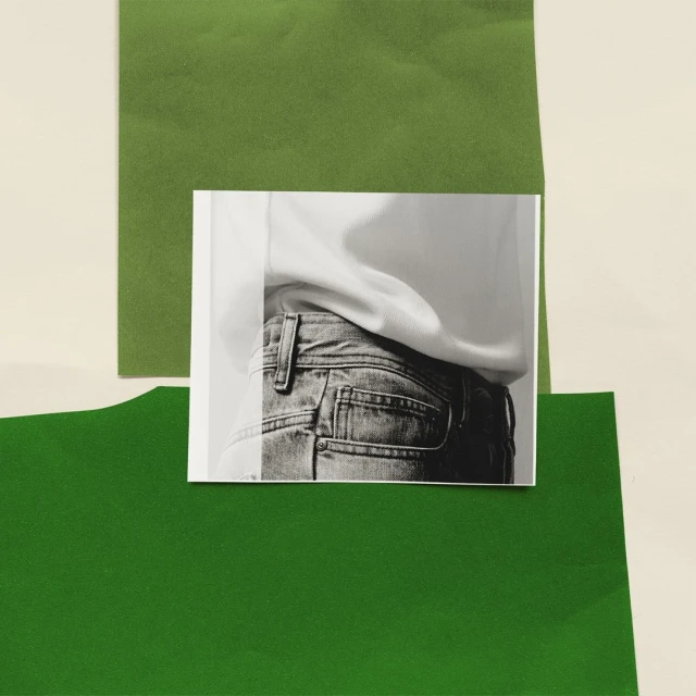 Cropped monochrome photograph on paper depicts person in jeans with white top, displayed against cream and green paper background.