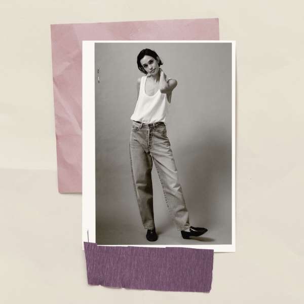 Black and white portrait photo of a young adult female posing in a white tank top and jeans against a neutral background.