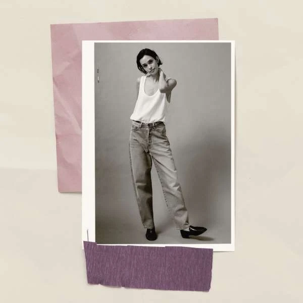 Black and white portrait photo of a young adult female posing in a white tank top and jeans against a neutral background.