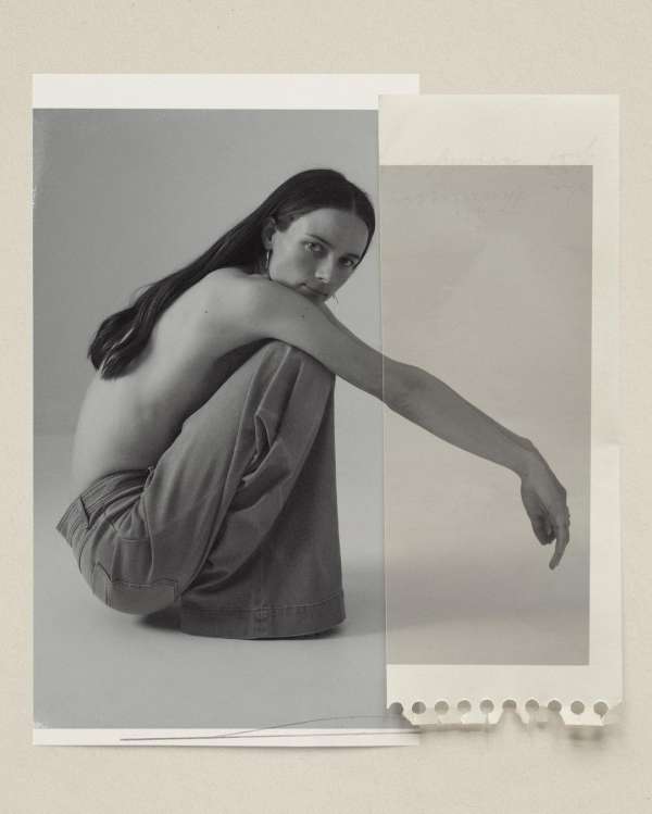 Monochrome portrait of a young adult woman with long dark hair, posing in wide-leg pants against overlapping paper backgrounds.