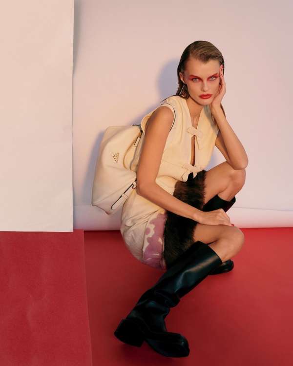 Model wearing a cream dress and black boots crouching against a studio backdrop, by illustrator Martin Cole.