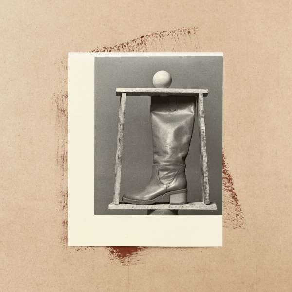 Artistic studio shot of a beige leather boot on a wooden stand, isolated on a cream and tan backdrop with textured paint strokes.