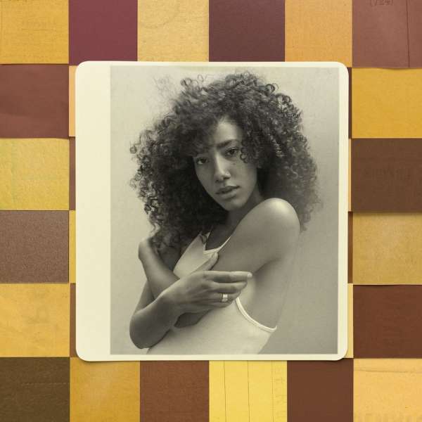Indoor portrait of a young adult female with curly hair, fair complexion, light tank top, and neutral expression, set against a textured background.
