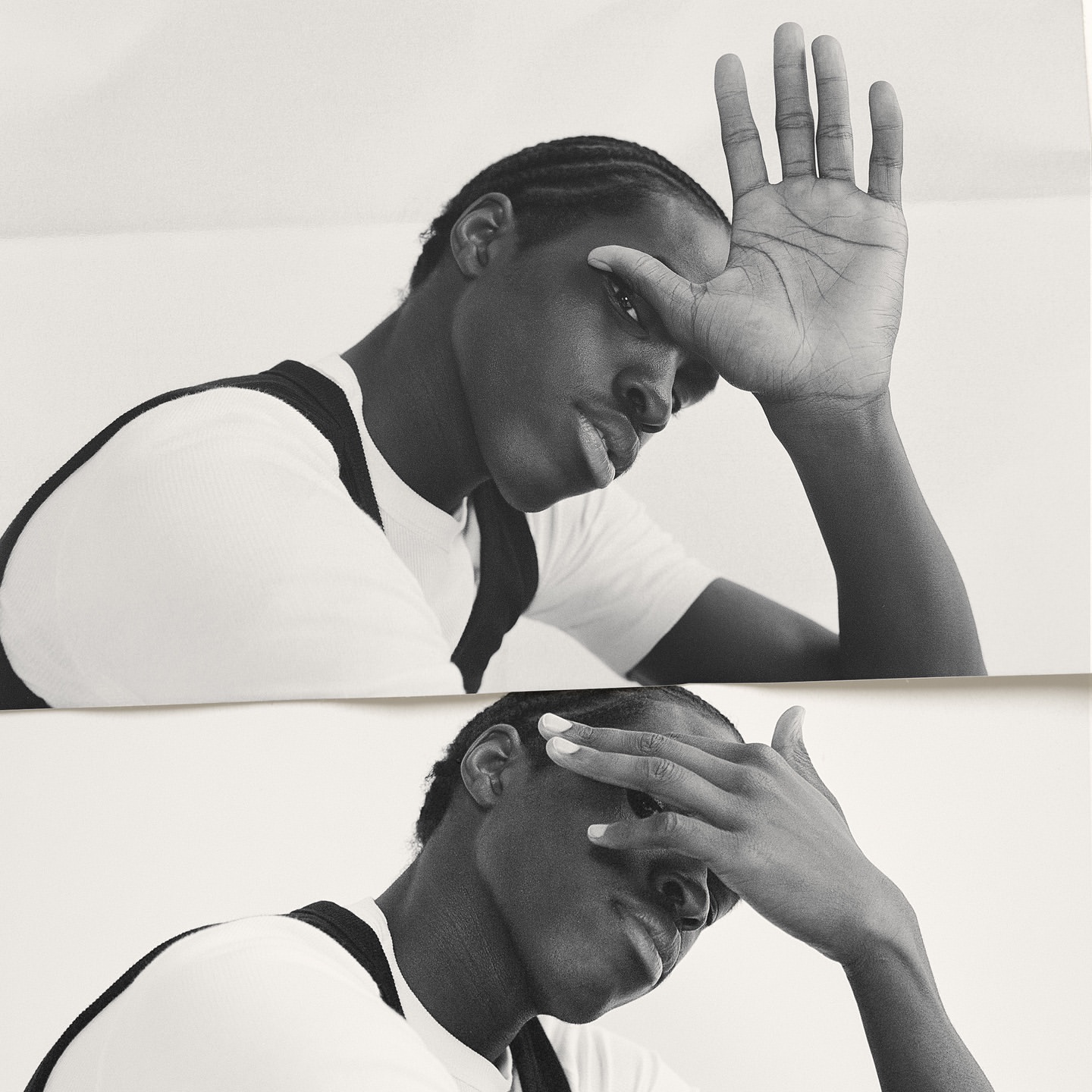 Black and white portrait of a black man with cornrows, partially covering his face with his hand in a reflective double exposure.