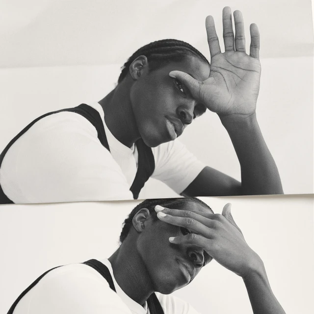 Black and white portrait of a black man with cornrows, partially covering his face with his hand in a reflective double exposure.