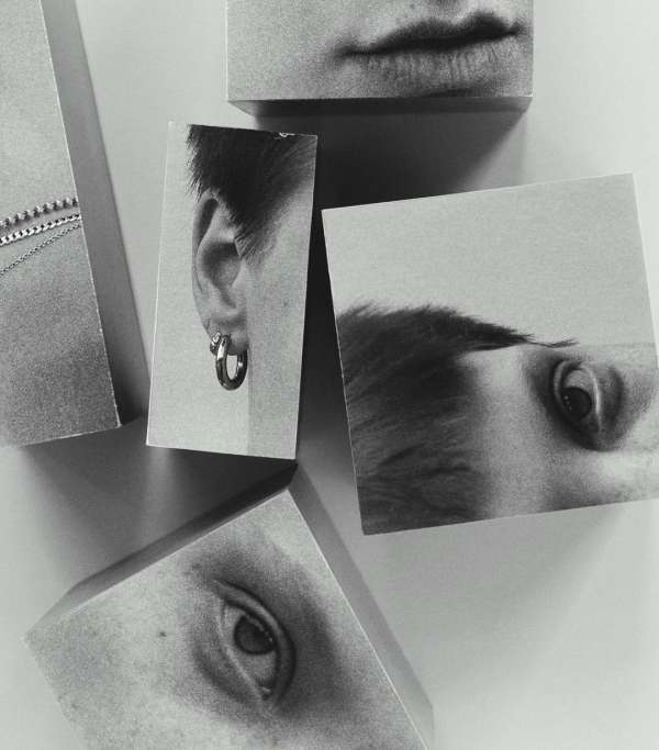 Monochrome artistic composition of human facial features on blocks; eye, ear with earring, mouth and partial necklace on white background.