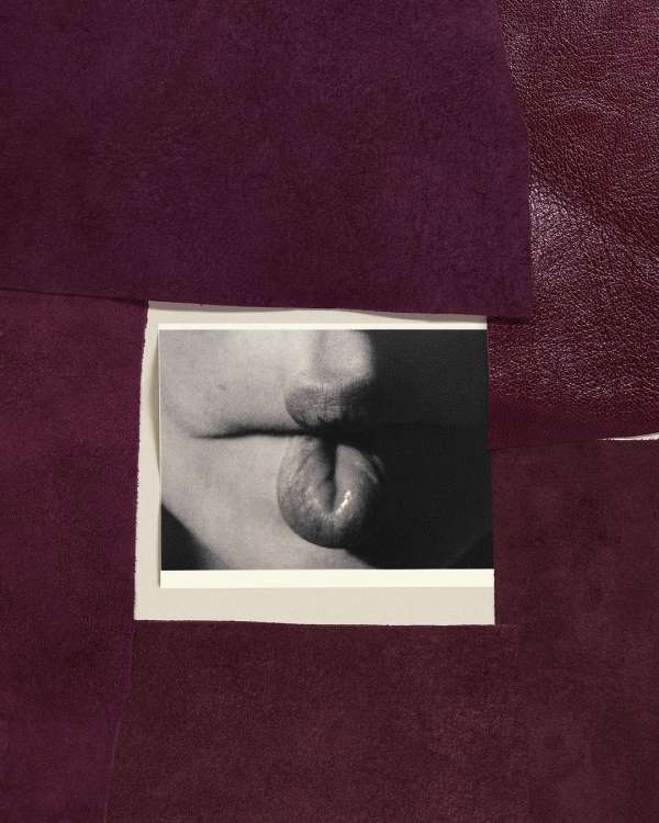 Close-up black and white photo of a person sticking their tongue out, positioned in front of textured purple fabric.