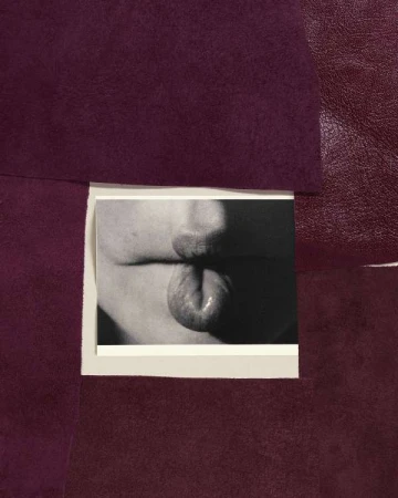 Close-up black and white photo of a person sticking their tongue out, positioned in front of textured purple fabric.