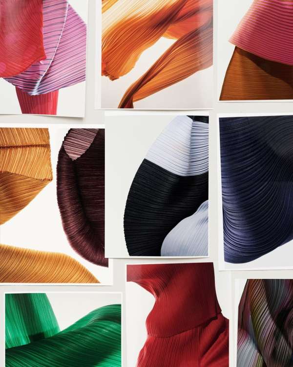 Abstract display of folded, colorful pleated fabric in shades of red, orange, blue, green, black, pink, and gold against a white backdrop.