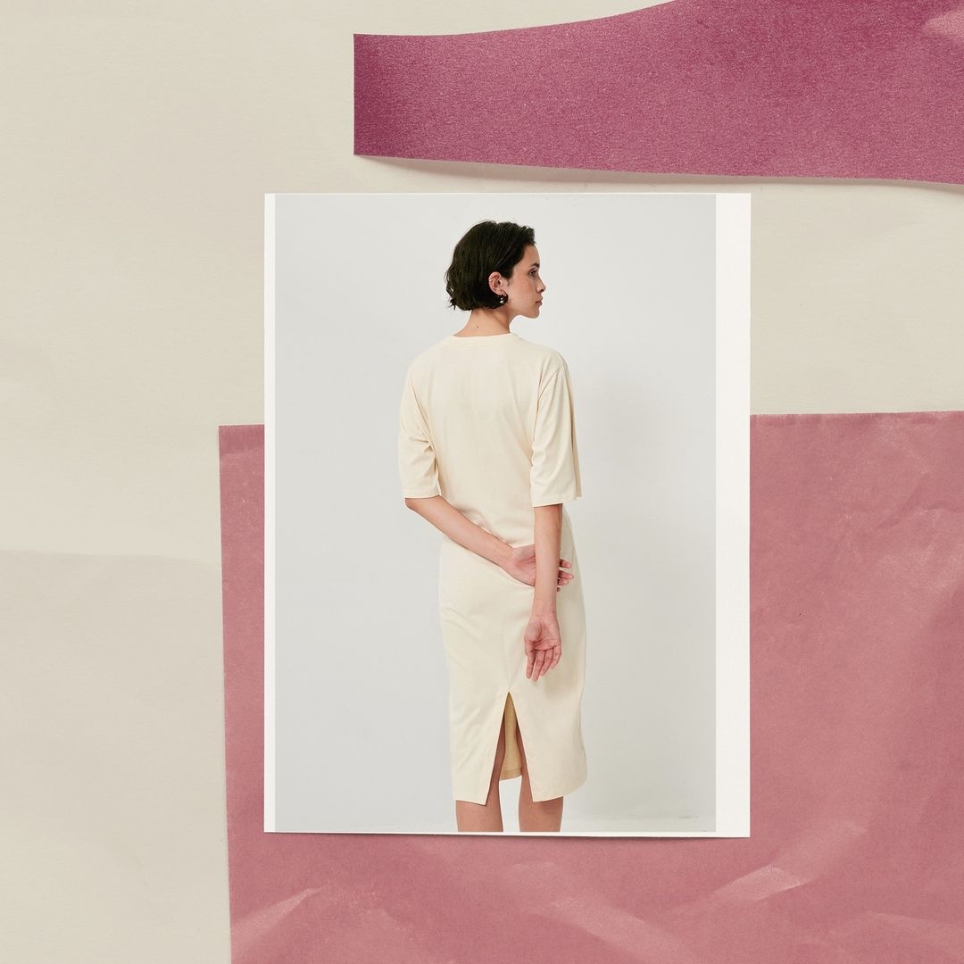 Woman in cream dress standing against a white square. The background is pink and cream. Fashion editorial with unique composition.