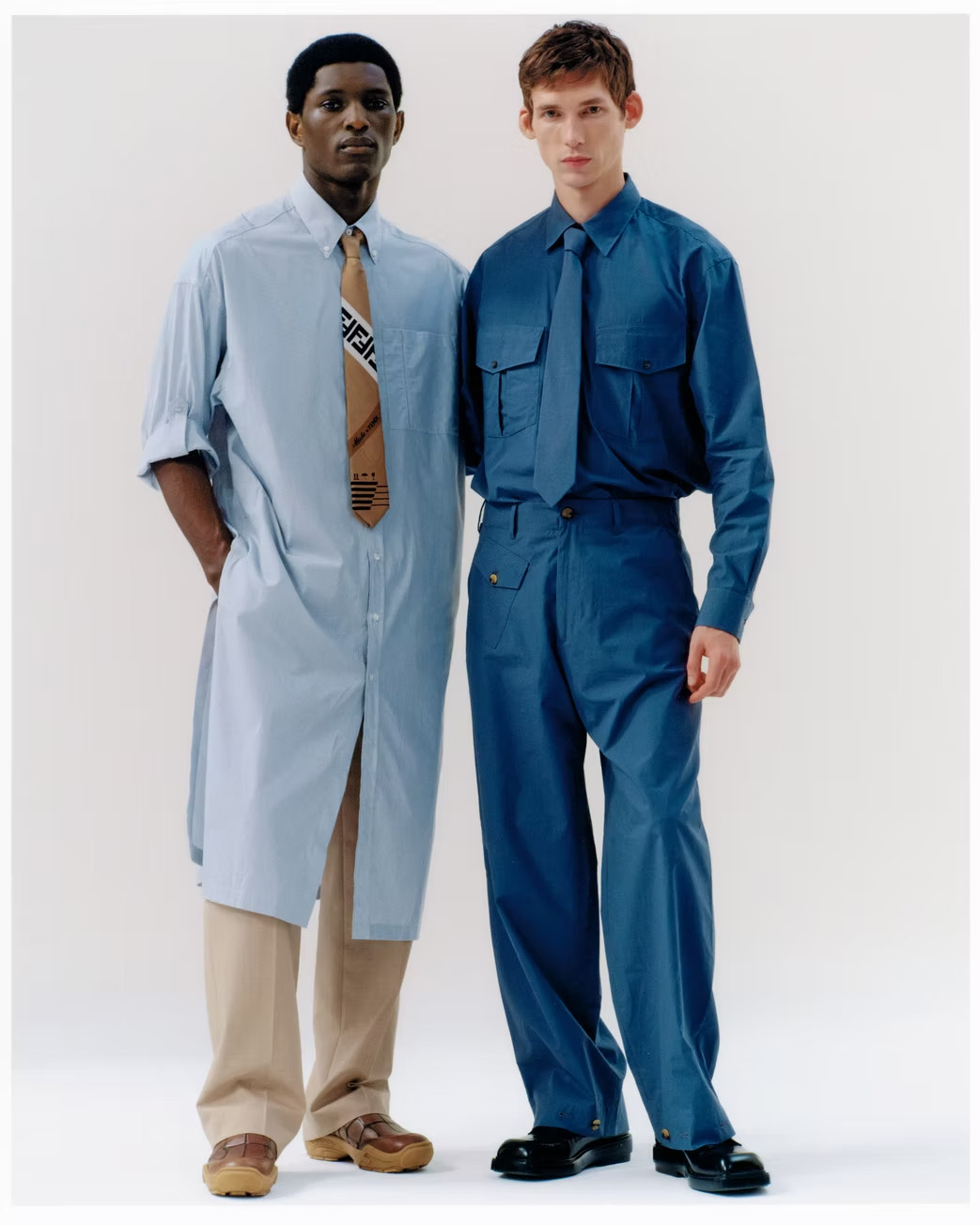 Two men pose in shirts, ties, and trousers against a white backdrop, showcasing contemporary fashion with a focus on design and style.