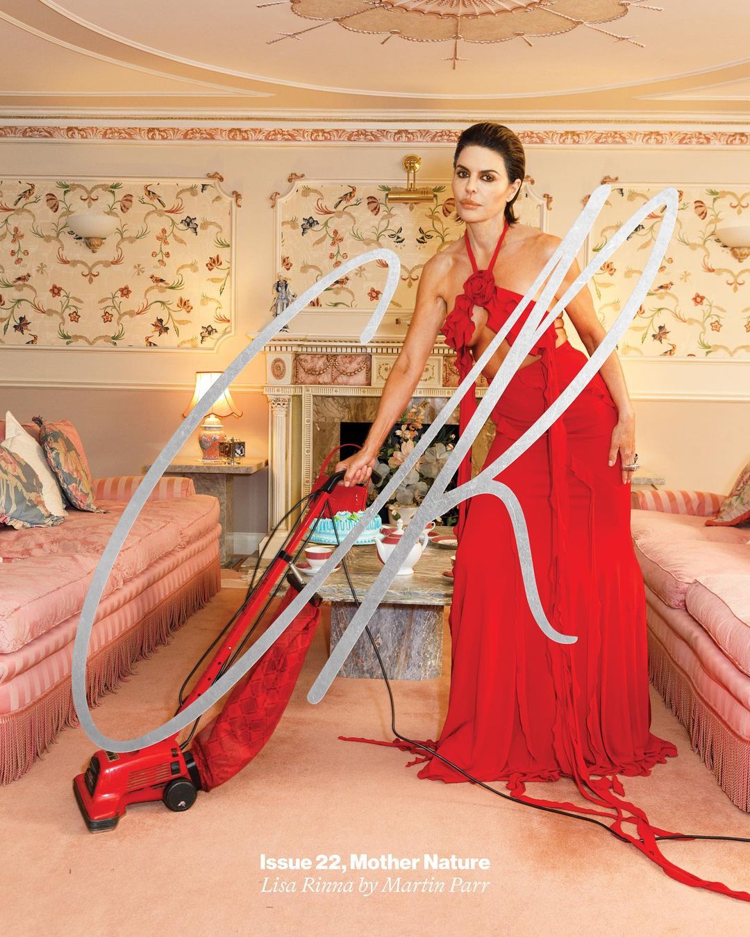 Elegant adult woman in a red gown vacuuming in a lavishly decorated interior, photographed for a magazine cover.