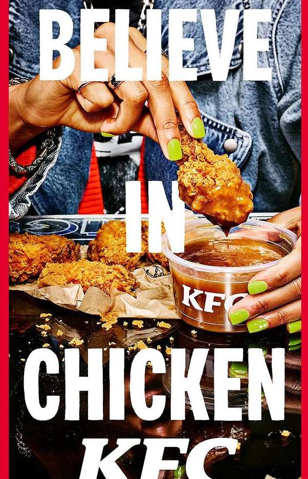 Close-up of a person holding a KFC fried chicken drumstick over a container of dipping sauce, with more chicken pieces on a plate.