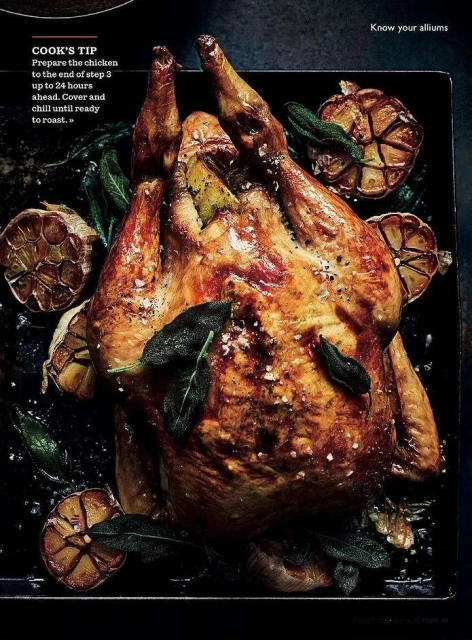 Roasted chicken on a dark tray, garnished with garlic cloves and sage leaves, presented with a warm, inviting lighting for a food-themed image.